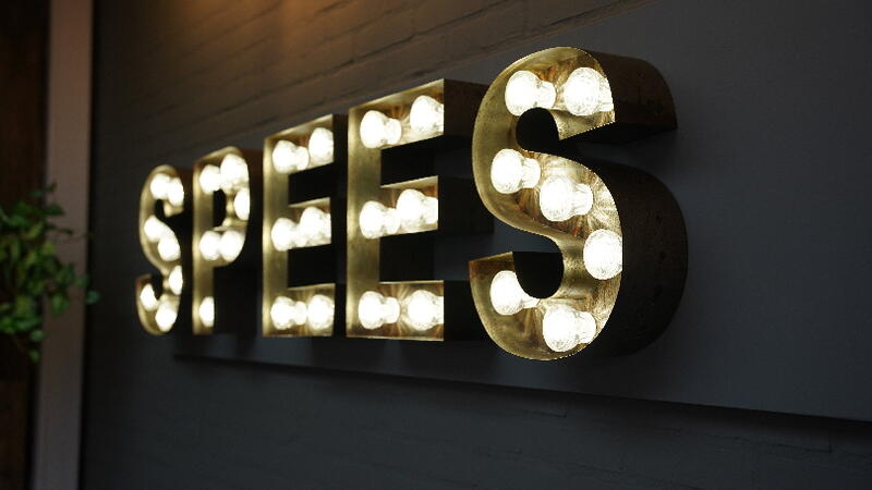 Lichtgevende letters "SPEES" aan de muur