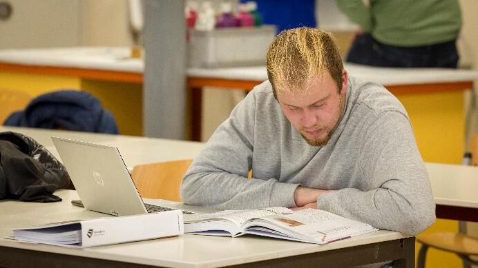 Een student zit in de schoolbanken en leest een studieboek