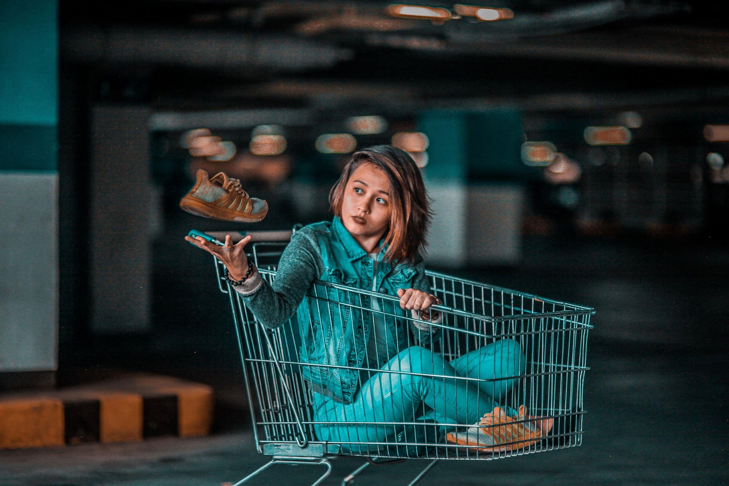 Een jongedame zit in een winkelwagentje en bewondert een paar trendy sneakers