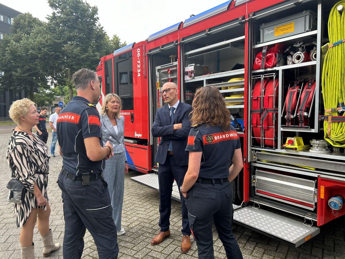 Ellen Marks en Petjo Molenaar staan voor een bluswagen te praten met leden van het brandweerkorps