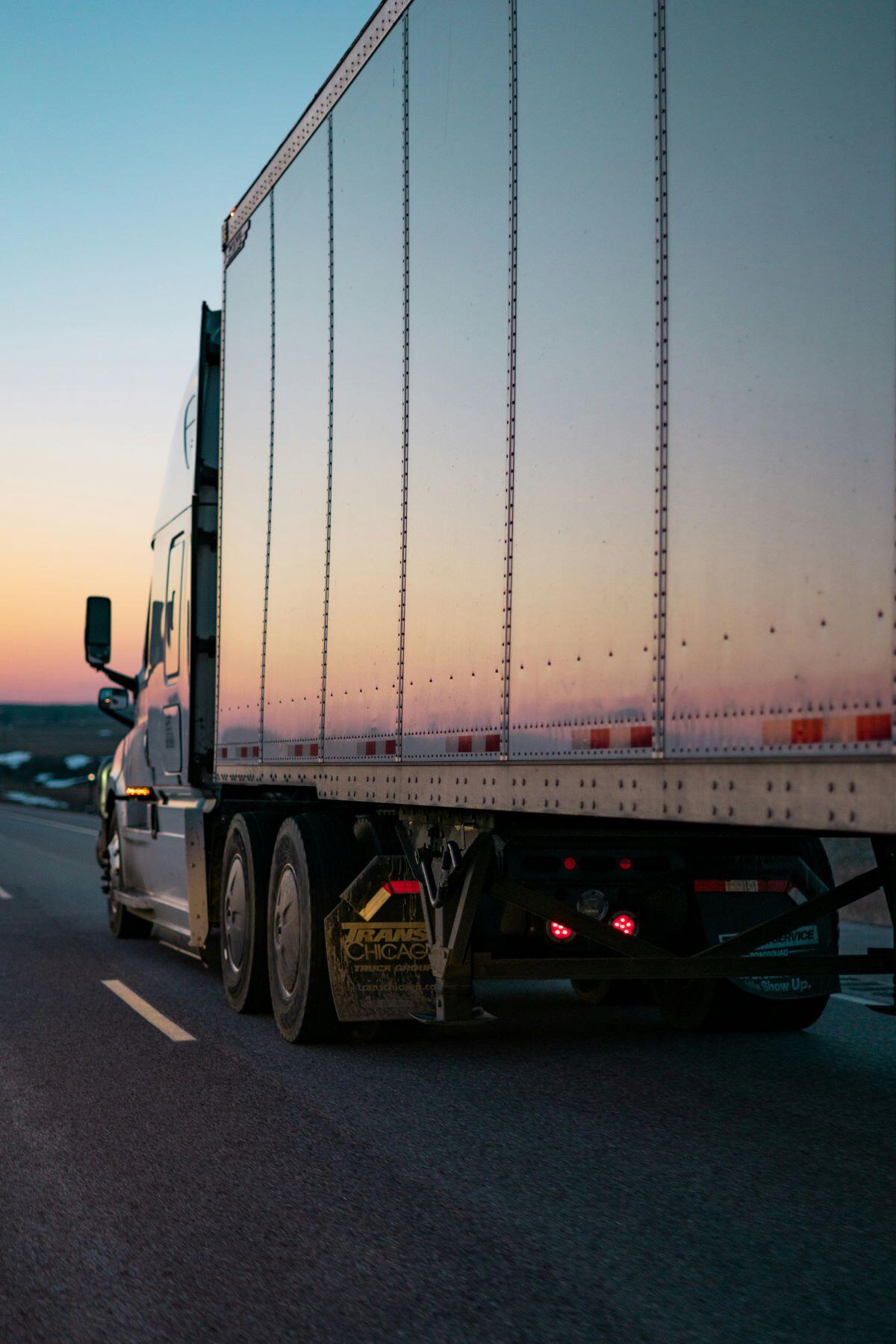 Vrachtwagen op de weg met een aanhanger waarop het zonlicht van een ondergaande zon reflecteerd