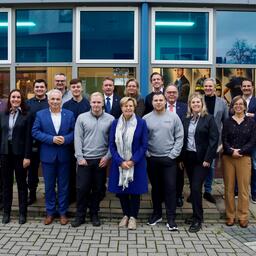 De wethouders van Apeldoorn staan met z'n allen voor het Aventus-gebouw aan Musschenbroekstraat